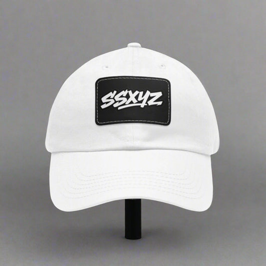 White dad hat with a black rectangular patch on the front displaying the white text "SSXYZ", the shorthand logo for Stylesavvy.xyz. The hat has a curved brim and an adjustable back strap.